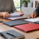 Two people organising several unbranded pension folders into one financial overview